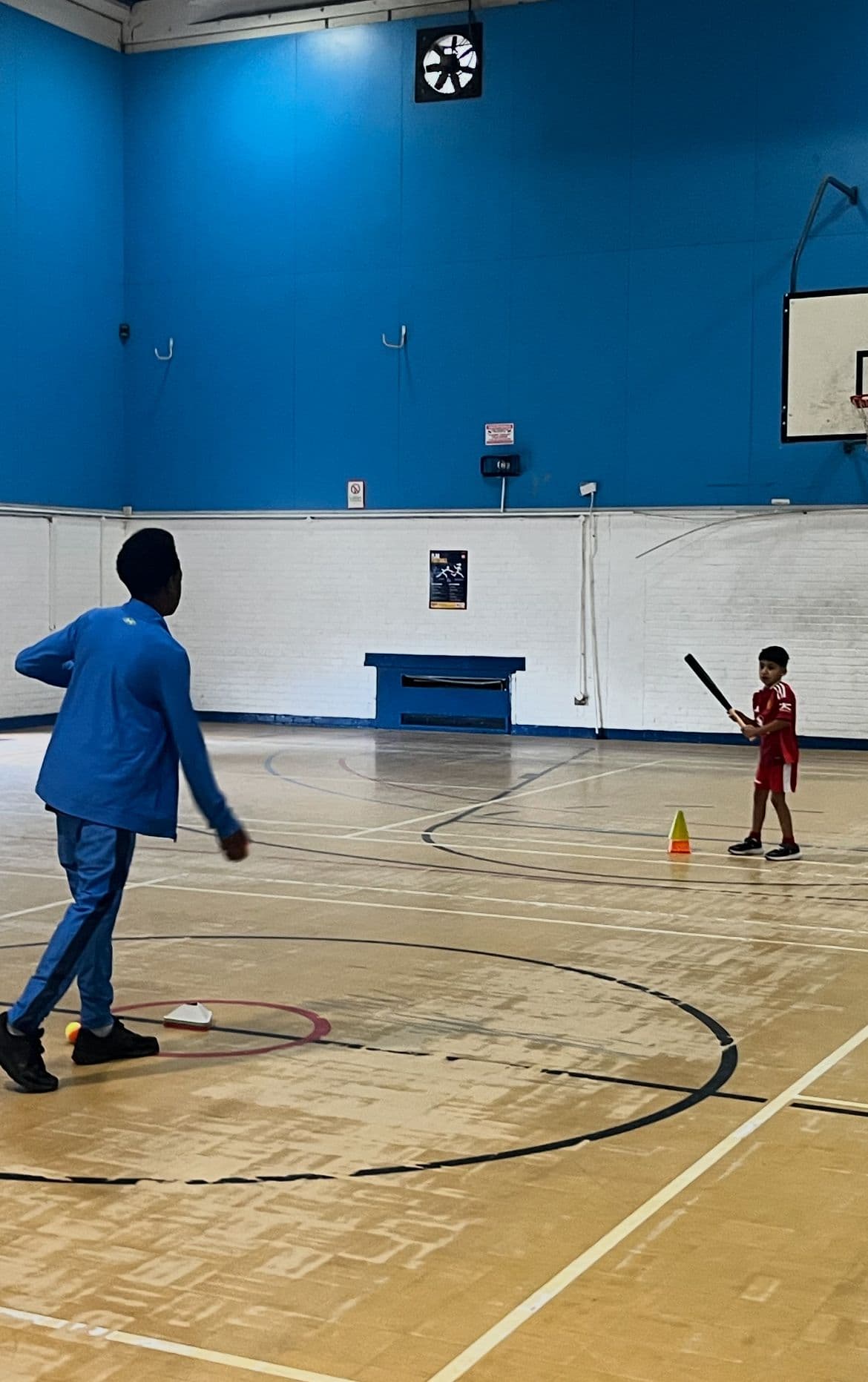 A coach bowling underarm to a young batter at indoor rounders